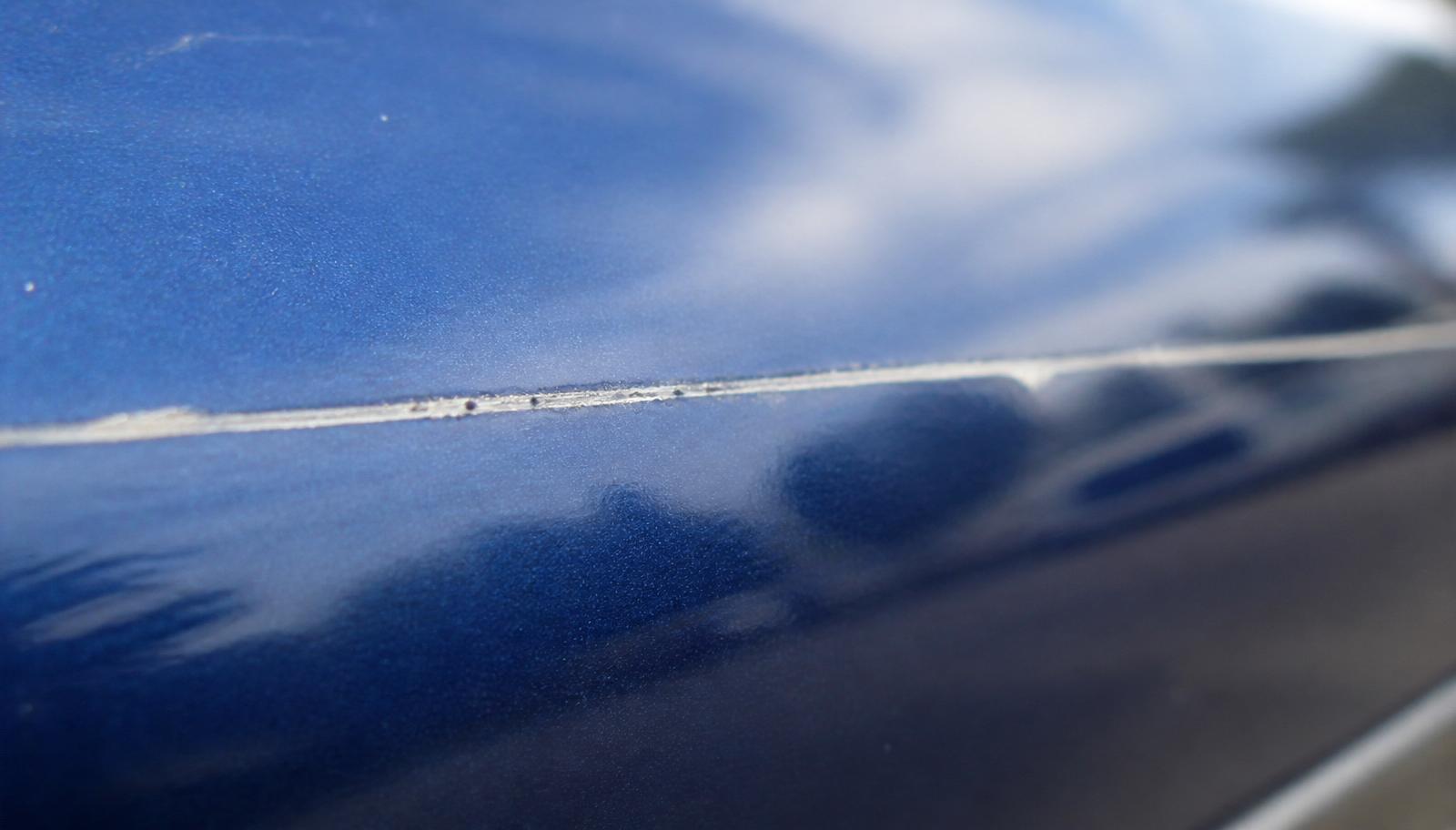 Long thin key scratch cutting through the clear coat of a glossy dark blue car door