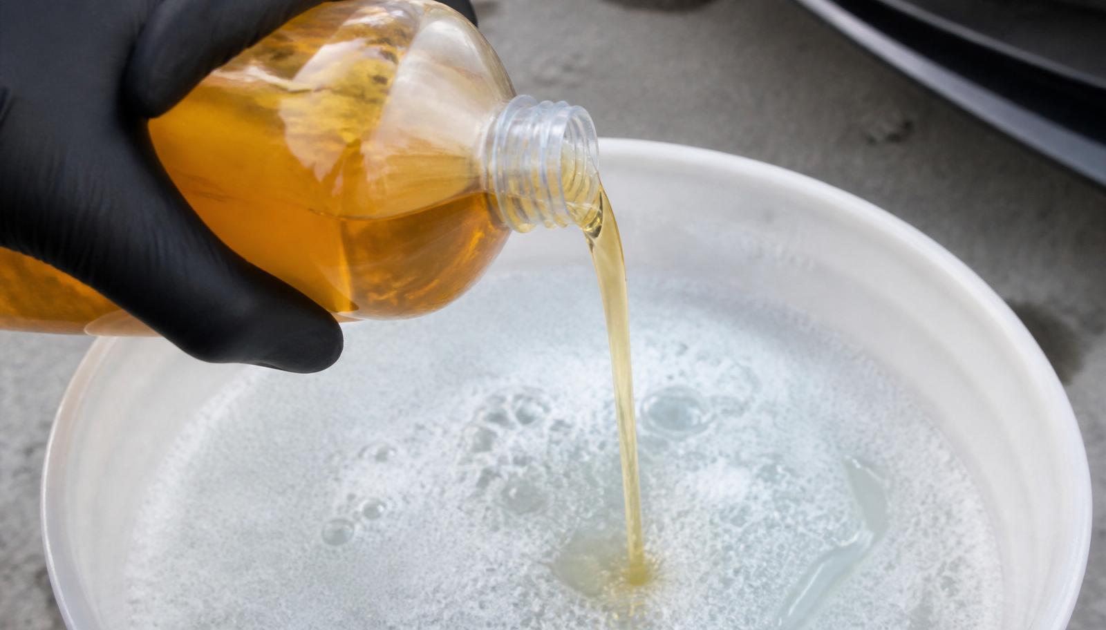 Gloved hand pouring pH-neutral car shampoo from a bottle into a bucket of water