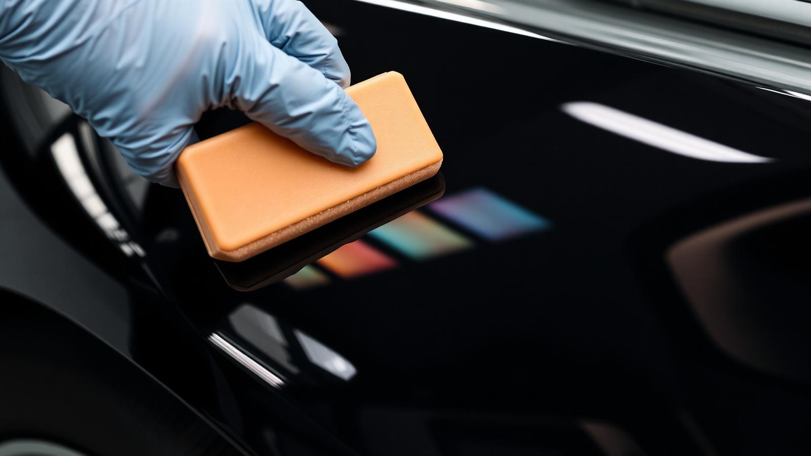 Gloved hand applying ceramic coating with an applicator block onto a black car fender